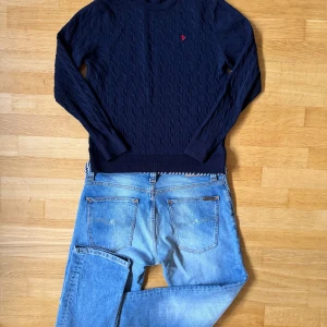 Mörkblå kabelstickad tröja Morris S - Snygg mörkblå kabelstickad tröja från Morris i 100% merinoull. Tröjan har rund hals, lång ärm och en röd broderad logga på bröstet. Perfekt för dig som gillar klassisk stil med en modern twist. Priset kan diskuteras vid snabb affär och om dubbar några funderingar är det bara att höra av sig🫡