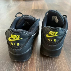 Nike Air Max svarta sneakers, strl 44 - Svarta Nike Air Max sneakers med neongula detaljer på loggan och tungan. Skorna har klassisk mesh och syntet på ovandelen, snörning och en vit swoosh på sidan. Snygg och sportig modell som passar perfekt till streetwear och vardagsstil. Gott skick används inte längre 