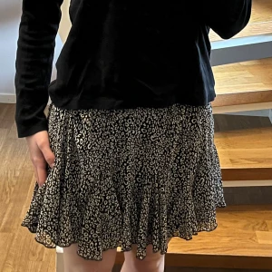 Svart leopardmönstrad kjol Retro Icone - Supersnygg kort kjol från Retro Icone med svart och vit leopardmönster. Kjolen har volangkant nedtill och ett elastiskt midjeband som gör den bekväm och enkel att bära.