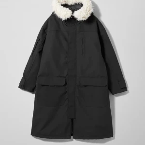 Svart Weekday oversized unisex med fuskpäls - Svart lång parkajacka från Weekday, modell Martha Parka. Jackan har en stor huva med vit fuskpäls, praktiska fickor framtill och justerbar midja baktill. Materialet är bomull och polyester, perfekt för kalla dagar. Stängs med dragkedja och har långa ärmar. Storlek S men känns snarare M/L.