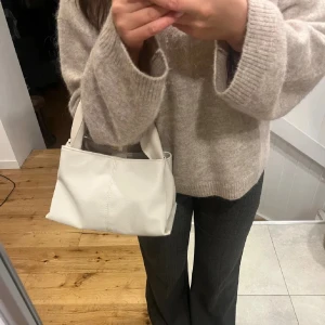 Beige handväska i skinnimitation - Stilren beige handväska med mjuk, fyrkantig form och breda handtag. Väskan är tillverkad i skinnimitation med diskreta sömmar och har en minimalistisk look som passar till många outfits. Perfekt storlek för det viktigaste du vill ha med dig.
