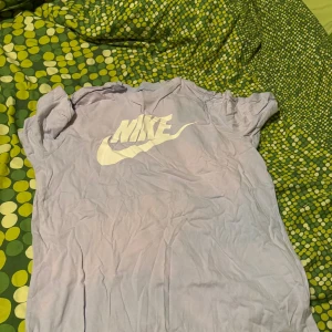 Ljuslila Nike t-shirt med logga - Säljer en ljuslila t-shirt från Nike med stor vit logga på bröstet. T-shirten har klassisk rund hals och korta ärmar, perfekt för dig som gillar sportiga och stilrena plagg. Materialet är mjuk bomull som känns skönt mot huden.
