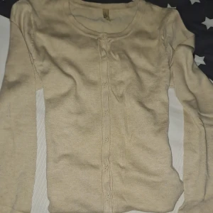 Beige kofta med knappar - Snygg beige kofta med rund hals och långa ärmar. Koftan har knappar hela vägen framtill och är tillverkad i ett mjukt stickat material som känns skönt mot huden. Perfekt att slänga på sig när det är lite kyligt ute. Sitter bra i midjan och speciellt till brunt hår