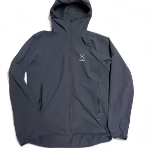 Svart vindjacka från Haglöfs dam L - Svart vindjacka från Haglöfs i dammodell, storlek L. Jackan har huva, två sidofickor med dragkedja och hel dragkedja framtill. Materialet är slitstark syntet och jackan har en stilren look med diskret Haglöfs-logga på bröstet. Perfekt för uteliv och äventyr.