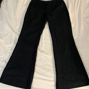 Mörkblå randiga kostymbyxor från gina tricot - Säljer ett par mörkblåa kostymbyxor från gina tricot med vita tunna ränder. Byxorna har låg midja, lätt bootcut ben och klassisk dragkedja med hake och knapp. Snyggt skräddad look och perfekt för dig som gillar en stilren vibe.