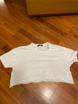 Vit croppad t-shirt från Bik Bok - Enkel och stilren vit croppad t-shirt från Bik Bok. T-shirten har korta ärmar och rund halsringning. Perfekt basplagg att matcha med jeans eller kjol. Tillverkad i mjuk bomull för skön känsla.