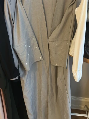 Ljusgrå abaya med månmönster - Säljer en ljusgrå abaya med vida ärmar och vita månmönster på ärmsluten. Perfekt för dig som gillar unika detaljer och minimalistisk stil.🩶