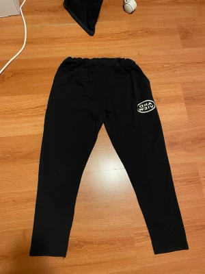 Svarta mjukisbyxor med tryck - Svarta mjukisbyxor med resår i midjan och vita tryckdetaljer fram och bak. På framsidan står det 'AND VIEW' och på baksidan 'FANSTLCPI'. Byxorna har en avslappnad passform och är perfekta för chill dagar. Tillverkade i mjukt bomullsmaterial.