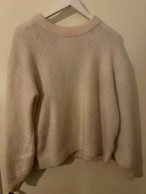 Vit stickad tröja med rund hals - Mysig beige stickad tröja med rund halsringning och ribbade muddar. Perfekt för kyliga dagar och enkel att matcha med olika outfits. Långärmad och har en avslappnad passform som ger en skön och trendig look.