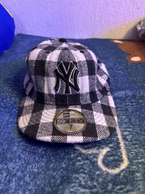 Rutig New Era Yankees keps - Säljer en svartvit rutig New Era 59FIFTY keps med Yankees-logga framtill. Klassisk flat brim och broderade detaljer på sidan och bak. Skön och stilren keps i mjukt tyg, perfekt för dig som vill sticka ut lite extra.