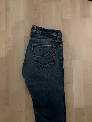 Jacob Cohën 622 Comfort blå jeans - Säljer ett par Jacob Cohën 622 Comfort jeans i klassisk blå tvätt med snygga slitningar och kontrastsömmar. Jeansen har raka ben, knappgylf och detaljerade fickor. Tillverkade i mjukt jeansmaterial för extra komfort och stil.