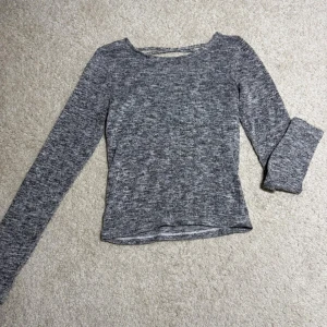 Gråmelerad långärmad topp XS - Säljer en gråmelerad långärmad topp i mjukt material. Toppen har en snygg v-ringning med snörningsdetalj som ger en extra touch. Passformen är normal och tyget är stretchigt och bekvämt. Perfekt till jeans eller kjol!