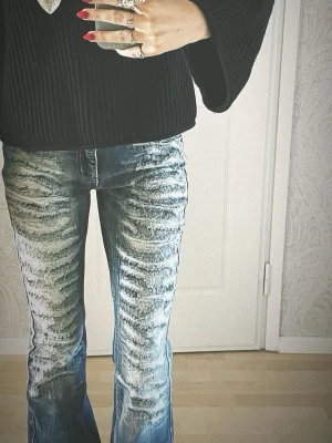 Blå bootcut jeans lågmidja jeans från Jaded London  - Säljer ett par blå bootcut jeans från JADED LONDON. Snygg design i midjan och ett tydligt mönster framtill. Jeansen har en klassisk femficksmodell och är tillverkade i slitstarkt denimtyg. Perfekta för dig som vill sticka ut med en unik look.
