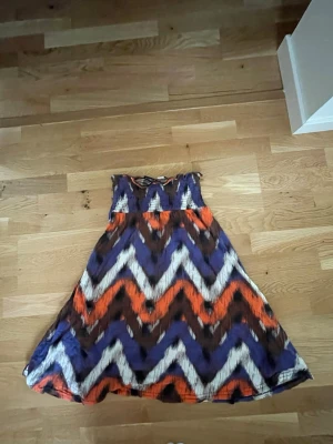 Mönstrad offshoulder klänning - En färgstark offshoulder klänning från H&M med zigzag-mönster i lila, orange, brun och vitt. Klänningen har smock upptill 