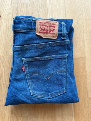 Levi's blå jeans straight fit - Klassiska blå Levi's jeans med rak passform och fem fickor. Jeansen har den ikoniska röda Levi's-lappen på bakfickan och patch i läder bak i midjan. Tillverkade i slitstarkt bomullsjeans med snygg tvätt och kontrastsömmar.