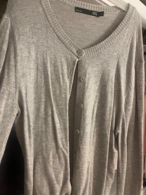 Grå kofta från 157 XS - Mysig grå kofta från 157 i storlek XS. Koftan har långa ärmar, ribbade muddar och knappar framtill. Perfekt att slänga över en topp för en chill look. Tillverkad i mjukt material som känns skönt mot huden.