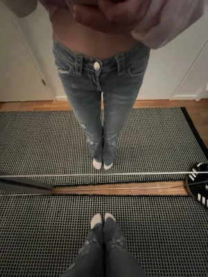 Blå bootcut jeans med broderade fickor - Säljer ett par blå bootcut low rise jeans med snygga slitningar och broderade detaljer på bakfickorna. Jeansen har normal passform och klassisk femficksdesign. Perfekta för dig som gillar en avslappnad men ändå trendig look.