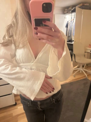 Vit omlottopp med vida ärmar - Säljer en superfin vit omlottopp med djup v-ringning och långa, vida ärmar. Toppen har knytband i ryggen vilken ger en trendig look. Lite stor på mig och säljer därför (lite dålig på att knyta rosetter😅) Men jätte fin detalj annars!💕