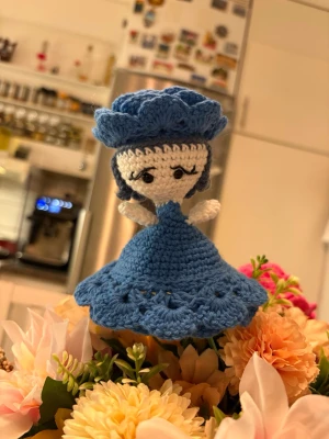 Handvirkad blomdocka - En vacker handvirkad blomma som kan vikas ut till en liten docka.   Varsamt skapad för hand med mycket kärlek och omsorg. Varje exemplar är unikt och passar perfekt som present, dekoration eller samlarobjekt. Blomdockan är virkad av min mamma, som lägger stor omsorg i varje stygn. Hör gärna av dig vid intresse ,pris kan variera beroende på utförande. Bilderna visar exempel på två varianter.  