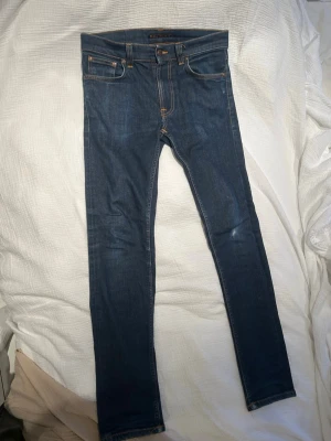 Nudie jeans herr W30/L32 - Säljer ett par mörkblå lean jeans från Nudie Jeans i storlek 30/32. Klassisk femficksmodell med orangea sömmar och Nudie-logga på bakfickan. Jeansen har en tight passform och är gjorda i slitstarkt denimtyg. Hör av er vid frågor
