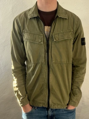Grön overshirt från Stone Island - Säljer en grön overshirt från Stone Island med klassisk patch på ärmen. Jackan har två bröstfickor med lock, dragkedja framtill och en avslappnad passform. Tillverkad i bomull och perfekt för lager på lager under vår och höst. Ny pris 4999kr, vårt pris 1699kr✅ skicket är som nytt, inga skador på jackan. Storlek S                  Hör av dig vid funderingar📩