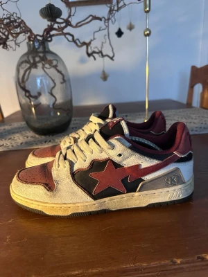 BAPE STA sneakers vinröd/svart/vit - Säljer ett par BAPE STA sneakers i vinrött, svart och vitt med den ikoniska stjärnan på sidan. Skorna har snörning, perforerad tå och lågt skaft. Materialet är en mix av mocka och skinn, vilket ger en schysst streetwear-vibe.
