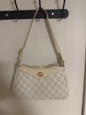 GG axelväska  - GG axelväska i en fin beige/cremefärg. Väskan har det klassiska GG-monogrammet, ljusa läderdetaljer och guldfärgade metalldelar. Öppen för bud. Hör gärna av dig vid frågor 🤍