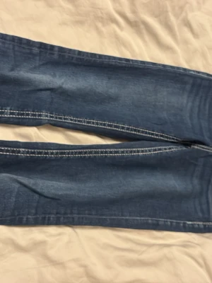 Blå jeans från Gina Tricot bootcut low waistet jeans 158  - Säljer ett par klassiska blå jeans från Gina Tricot i storlek 158. Jeansen har tydliga vita kontrastsömmar, bakfickor med lock och knapp, samt dragkedja framtill. Materialet är slitstarkt jeans och passformen är normal med raka ben.