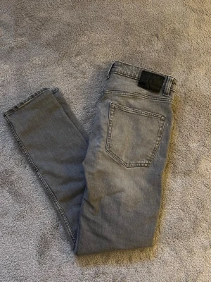 Grå slim jeans - Säljer ett par gråa slim fit jeans från lager 157 i storlek W28 L32. Jeansen har klassisk femficksdesign, raka ben och snygg tvättad look. Perfekta för dig som gillar en smalare passform och vill ha ett par stilrena jeans till vardags.