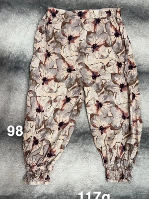 Blommiga byxor med resår i benslut - Säljer ett par ljusa byxor med stort blommönster. Byxorna har resår i midjan och vid bensluten för en skön och avslappnad passform. Perfekta för dig som gillar färg och mönster!🌸 Fint använt skick. Storlek 98
