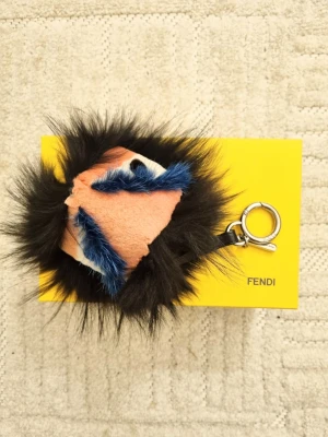 Fendi monster nyckelring charm - Säljer en fluffig och unik pälsboll från Fendi med ansiktsdetaljer i rosa, blått och svart. Nyckelringen har en metallring med Fendi-logga och är perfekt som accessoar till väskan eller nycklarna. Supercool detalj för dig som gillar statement pieces. Nypris 5800.