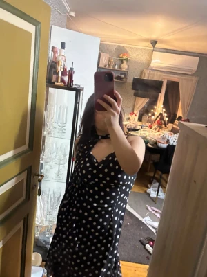 Svart lång prickig klänning - Säljer en svart långklänning med vita prickar och tunna axelband som knyts. Klänningen har en snygg draperad urringning och volangdetaljer nertill. Materialet känns lätt och flowy, perfekt för dig som vill sticka ut med ett klassiskt mönster. Köptes för 699