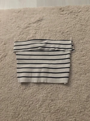 Randig bandeau tubtopp från FB Sister - Säljer en ribbad bandeau tubtopp från FB Sister i vitt med svarta horisontella ränder. Toppen är axelbandslös och har en croppad passform, perfekt för sommardagar. Materialet är stretchigt och mjukt, vilket gör den superbekväm att bära.