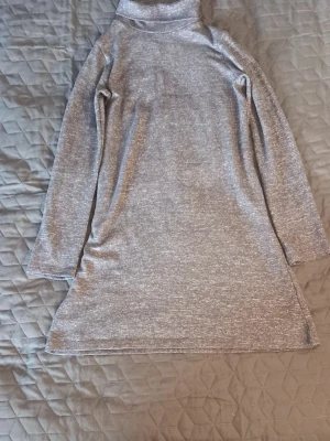 Grå polotröja/klänning i mjukt material - Mysig grå polotröja/klänning med lång ärm och rak passform. Tröjan är i ett mjukt, stretchigt material och har en klassisk polokrage. Perfekt för lager på lager under kyliga dagar. Enkel och stilren look som funkar till det mesta.