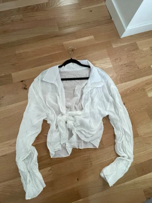 Vit knytblus/skjorta  - En vit, tunn och luftig blus/skjorta med lång ärm och stor krage. Skjortan är croppad och knyts framtill. Tror den är från Shein, storlek L