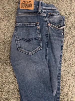 Replay blå jeans straight fit - Säljer ett par klassiska blå jeans från Replay med snygg tvätt och raka ben. Jeansen har fyrafickor då en har gått sönder, läderpatch bak och diskreta slitningar framtill för en cool look. Materialet är tåligt jeans i bomull och passformen är normal med straight fit. Riktigt najs för vardags bruk