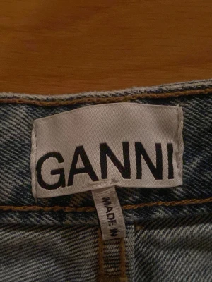 Blå raka jeans från Ganni - Säljer ett par klassiska blå jeans från Ganni med raka ben och mellan till hög midja. Jeansen har knappgylf med fyra knappar där den översta är rosa och resten är silverfärgade. De har även en liten slits i botten på båda benen. W24 L32