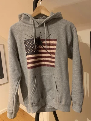 Grå hoodien från Concrete Ink, storlek S - Säljer denna tvär feta helt nya hoodie från Contrete Ink. Hoodien har ett riktigt schysst tryck där fram med en amerikans flagga i och en stilren svart fläck på. Hör av dig vid minsta fundering och pris kan diskuteras! 