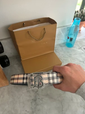 Rutig Burberry bälte med B-spänne - Snyggt burrbery bälte som går att vända på, kommer inplastat och helt oanvänt. Storlek 105cm box medföljer ej!