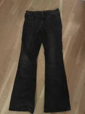 Svarta bootcut jeans från Denim Day - Säljer ett par svarta bootcut jeans från Denim Day i storlek 164. Jeansen har klassisk femficksdesign, normal midja och är tillverkade i ett mjukt jeansmaterial. Snyggt utsvängda ben för en trendig siluett.