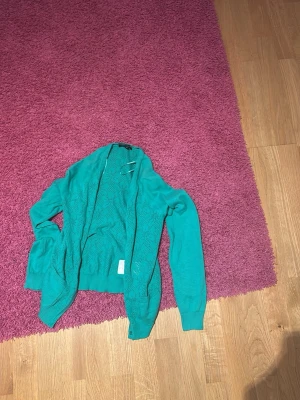 Turkos kofta från Bramante Collection - Säljer en turkos kofta från Bramante Collection i storlek S. Koftan har ett fint hålmönster, långa ärmar och små dekorativa knappar framtill. Perfekt att slänga över en topp för en chill look.