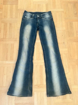 Blå bootcut jeans med slitningar✨✨💖 - Säljer ett par blå bootcut jeans med snygga slitningar och ljusa tvättade partier. Klassisk femficksmodell med låg mid sopassning och breda ben. Materialet är jeans i bomull och de har en cool vintage look. Lite slitna