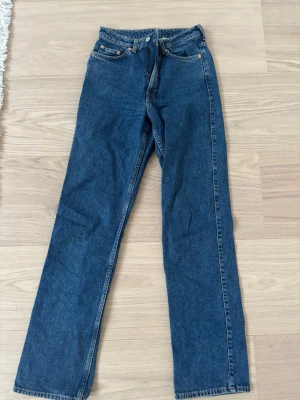 Weekday Rowe Extra High Straight Jeans - Säljer ett par mörkblå Weekday Rowe jeans med extra hög midja och raka ben. Klassisk femficksmodell i kraftigt denimtyg, perfekta för en clean och tidlös look. Storlek 26/34.