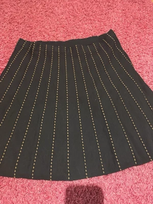 Svart kjol med beige ränder från Rabalder - Säljer en svart kjol från Rabalder i storlek S. Kjolen har beige lodräta ränder som ger en snygg och stilren look. Modellen är lätt utställd och har resår i midjan för skön passform. Perfekt att matcha med en enkel topp och boots.