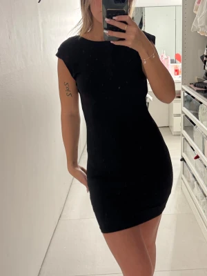 Svart tight kortklänning med öppen rygg - Säljer en svart, tight kortklänning med öppen rygg och korta ärmar. Klänningen har en enkel och stilren design som sitter snyggt på kroppen. Perfekt för dig som gillar minimalistisk stil och vill ha något som sticker ut med den öppna ryggen.