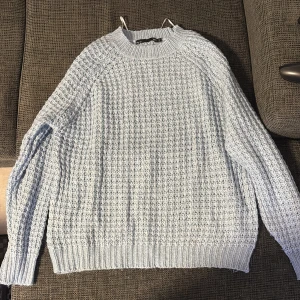 Ljusblå stickad tröja från 157 - Mysig ljusblå stickad tröja från 157 i storlek S. Tröjan har ett grovt stickat mönster och ribbade muddar vid ärmslut och nederkant. Perfekt för kyliga dagar och enkel att matcha med jeans eller kjol.