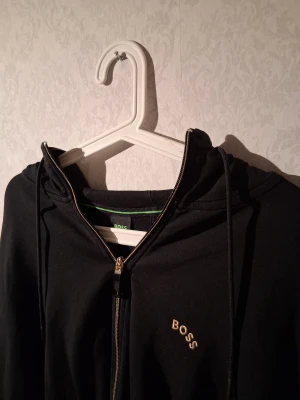Hugo Boss Hoodie Svart - Hoodien är väl använd men inget fel på den, det som kan sticka ut lite är ett litet hål i ryggen vid baksidan men man ser de knappast