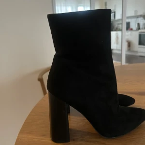 Svarta mocka stövletter med klack - Säljer ett par svarta stövletter i mjuk mocka med hög, bred klack och spetsig tå. Nya endast testade. Skorna har en stilren och minimalistisk design som passar perfekt till höst och vinter. Supersnygga till både jeans och kjol! 