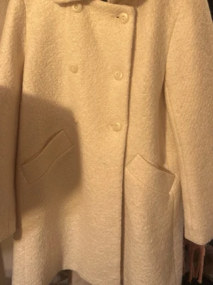 Beige skepparkavaj i ullmix - Säljer en beige skepparkavaj i ullmix med dubbelknäppning och stora fickor framtill. Jackan har en mjuk, lite fluffig yta och är helfodrad för extra värme. Perfekt för dig som vill ha en klassisk och stilren look under höst och vinter.