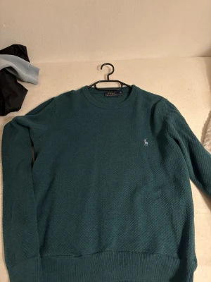 Mörkgrön stickad tröja Polo Ralph Lauren - Säljer en mörkgrön stickad tröja från Polo Ralph Lauren i storlek S. Tröjan har rund halsringning, diskret strukturmönster och den klassiska broderade loggan på bröstet. Perfekt till höst och vinter för en clean och stilren look.